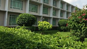 Un edificio de varios pisos con fachada simétrica, amplias ventanas y un jardín cuidado con diversos arbustos y plantas en flor.