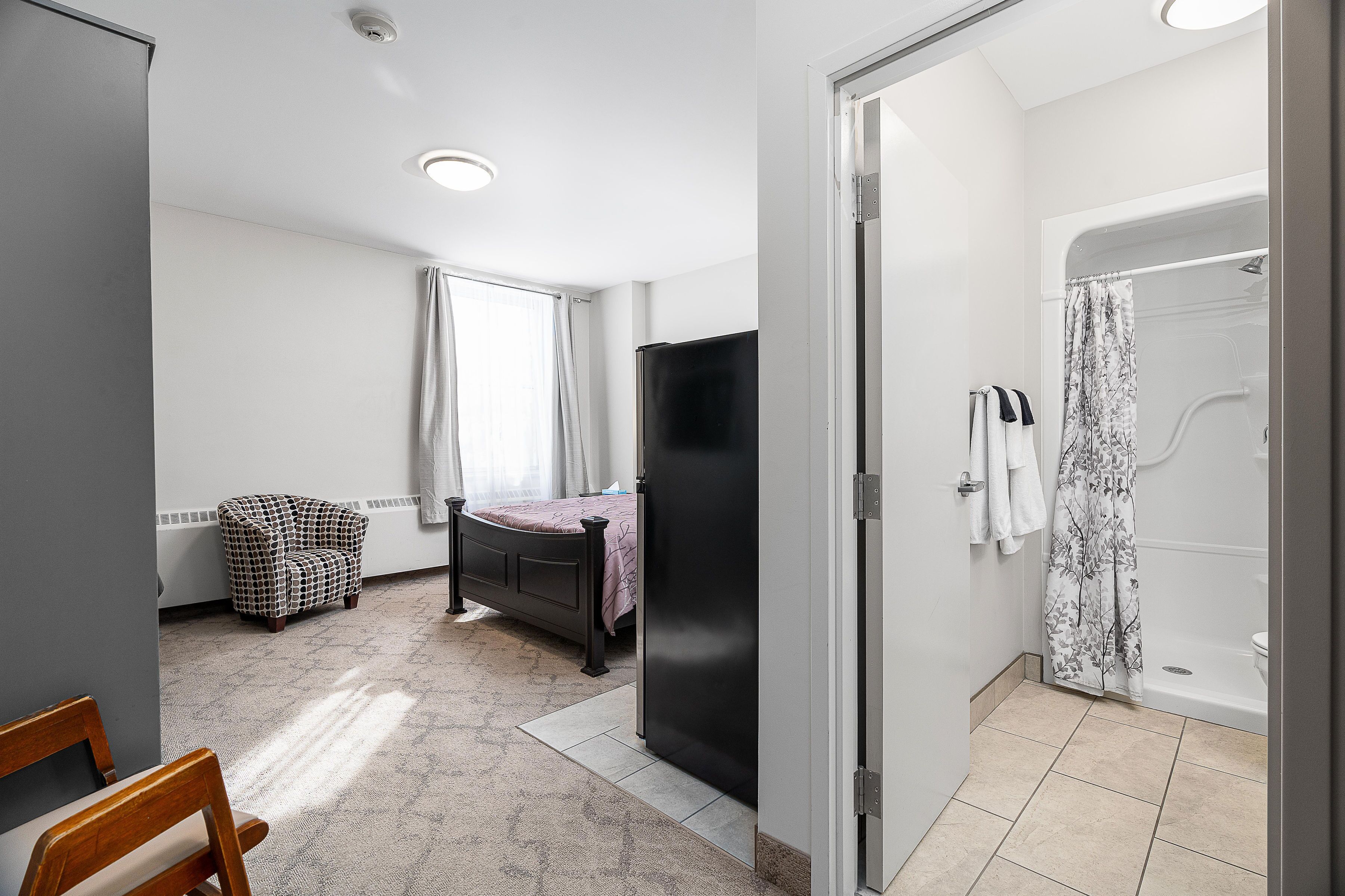 Un dormitorio con cama, una silla, armario y baño con bañera y ducha.