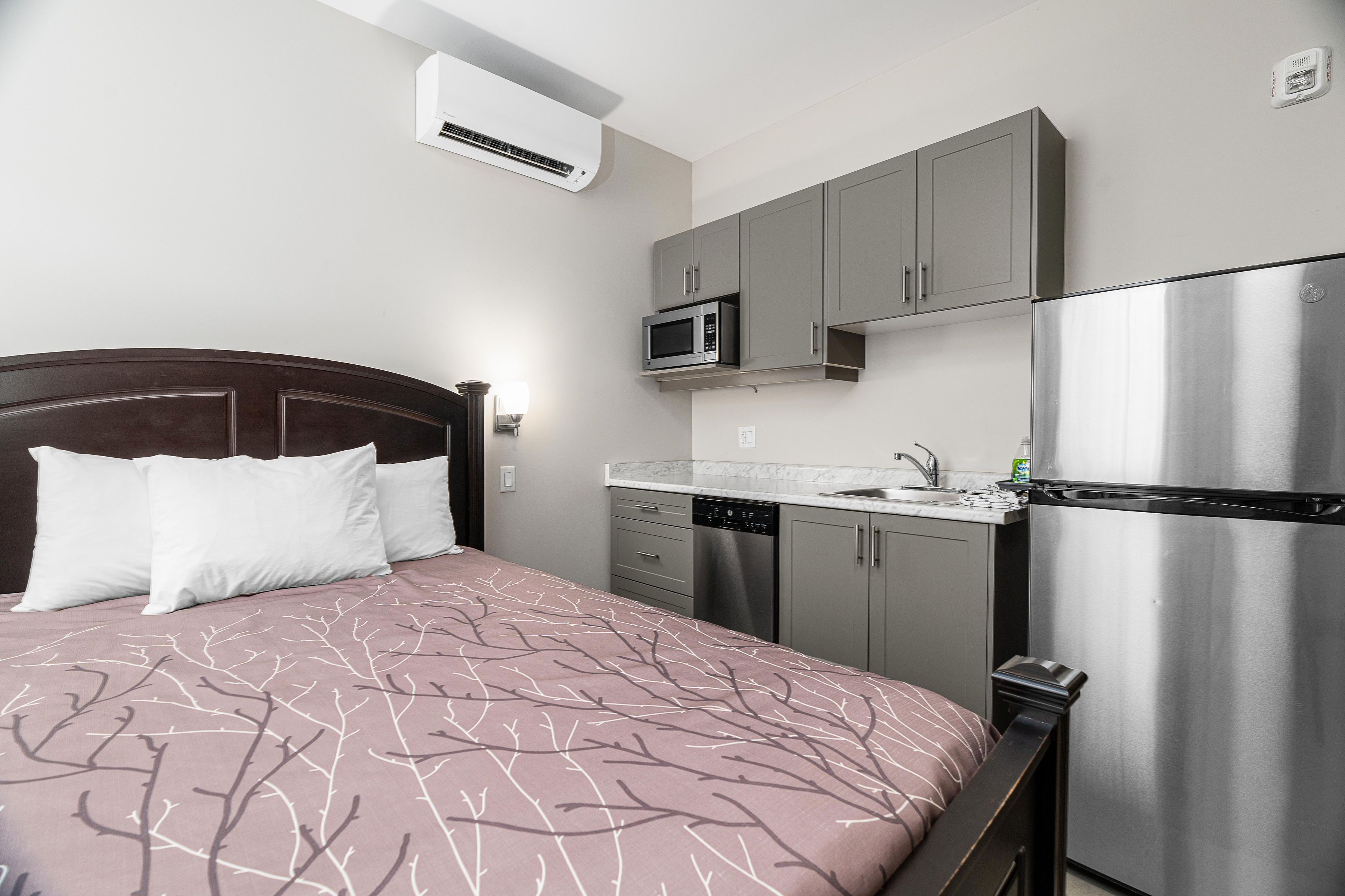 A bedroom with a bed, a microwave, a refrigerator, and a sink in a compact kitchenette.
