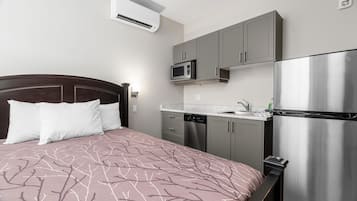 A bedroom with a bed, a microwave, a refrigerator, and a sink in a compact kitchenette.