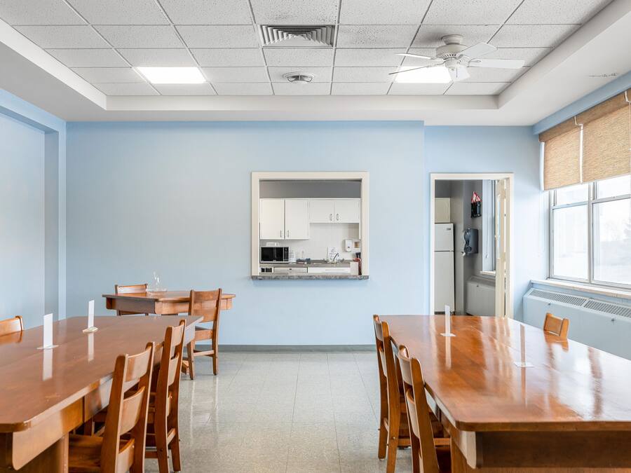 A conference room with a long wooden table, chairs, a kitchenette, and a window with blinds.