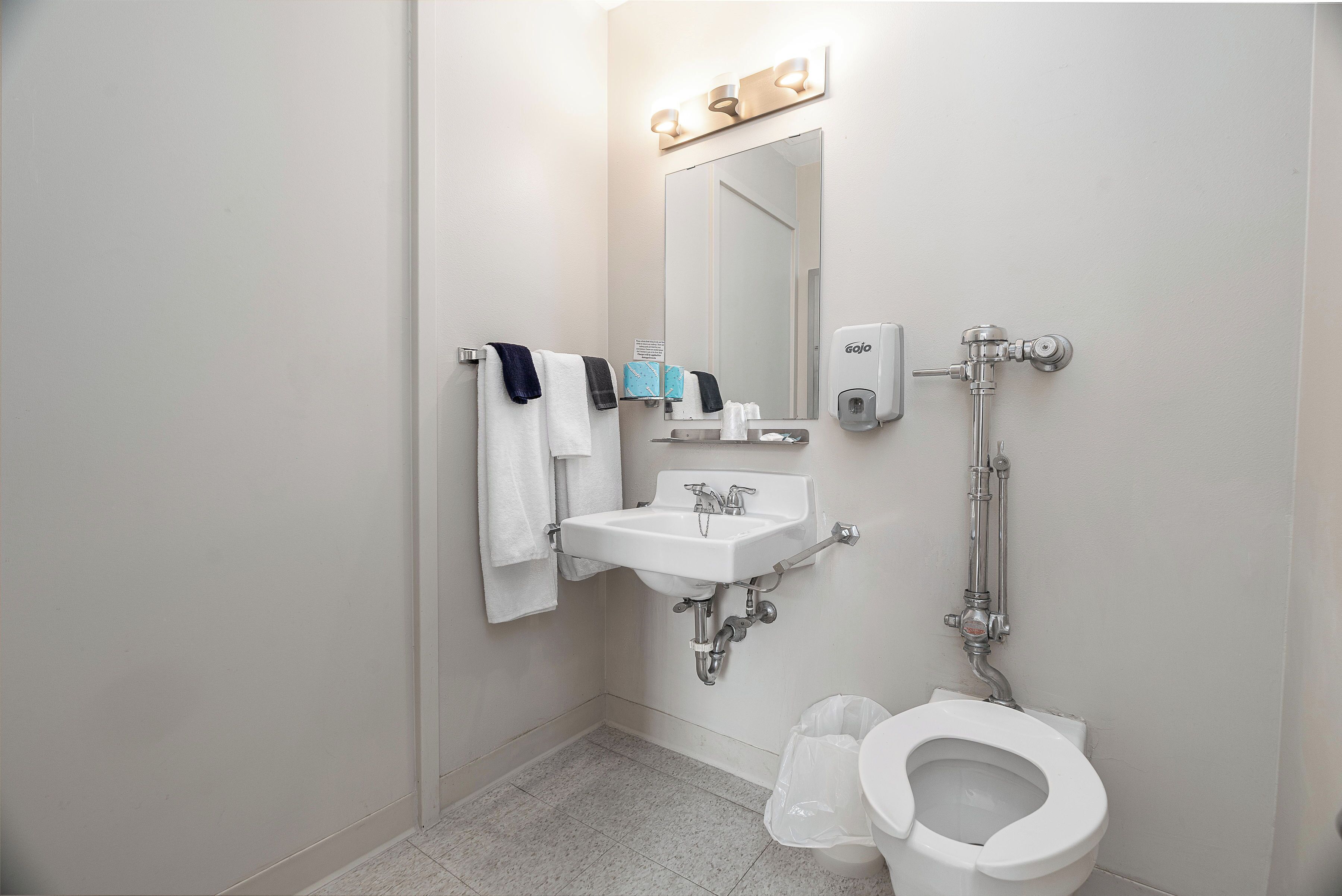 A bathroom with a sink, mirror, towel rack, toilet, and a soap dispenser.
