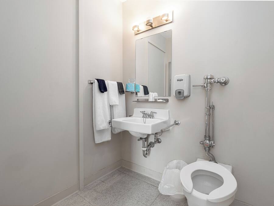 A bathroom with a sink, mirror, towel rack, toilet, and a soap dispenser.