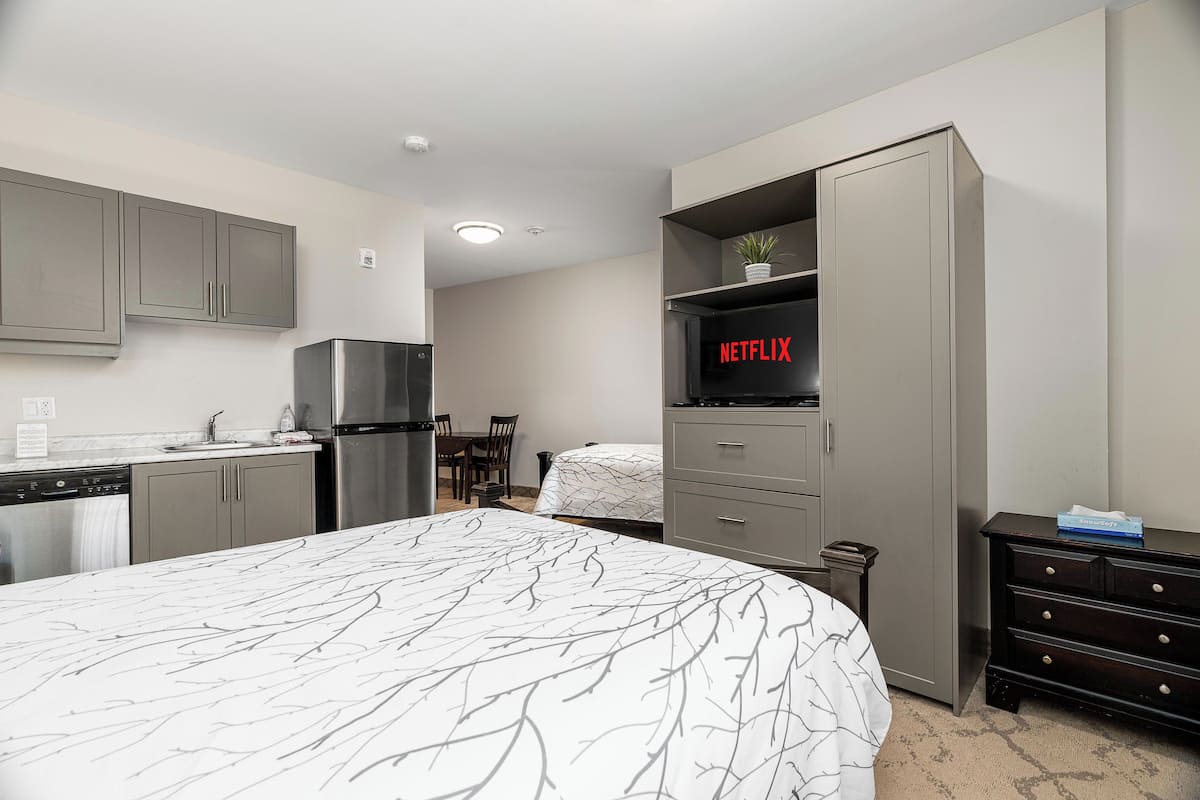 Une chambre d’hôtel moderne équipée d’un lit, d’une kitchenette et d’un téléviseur fixé à un meuble.