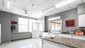 Una cocina con encimera de granito, armarios blancos, ventilador de techo y ventana con persianas.