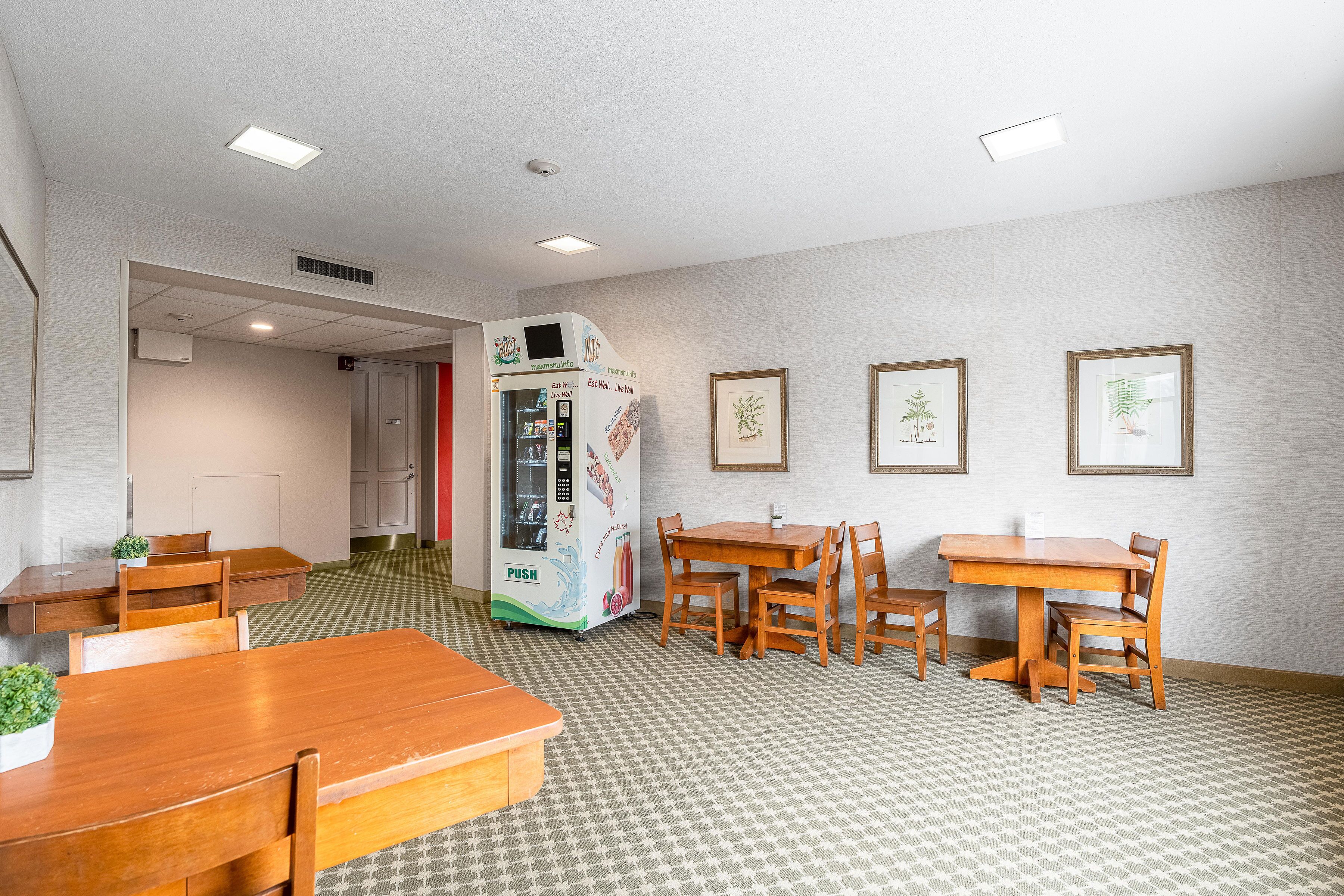 A dining area with wooden tables and chairs, a vending machine, and framed botanical prints on the wall.
