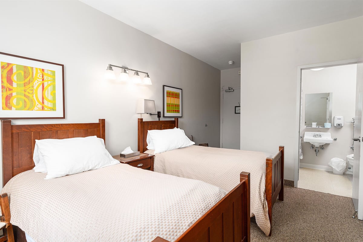 Une chambre d’hôtel avec deux lits, une table de chevet, une lampe et un tableau encadré au mur.