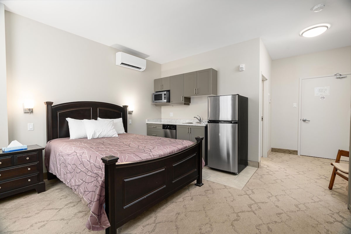 Une chambre comprenant un lit, une commode, un four à micro-ondes, un réfrigérateur et un petit coin cuisine.