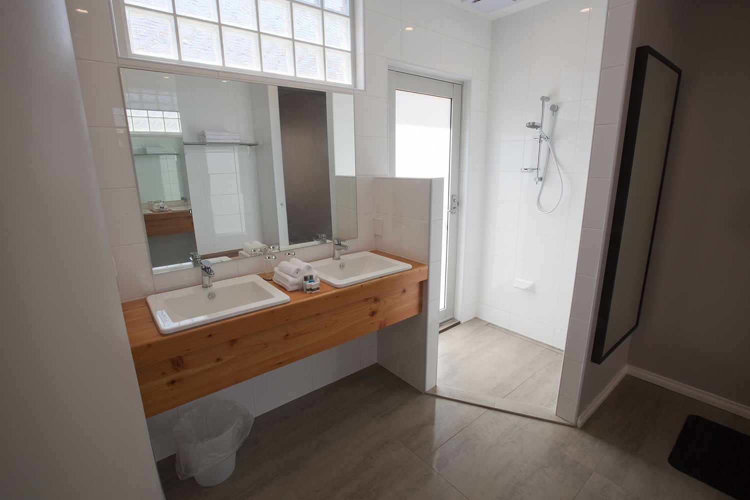 Ein modernes Badezimmer mit zwei Waschbecken, einem großen Spiegel und einer Dusche.