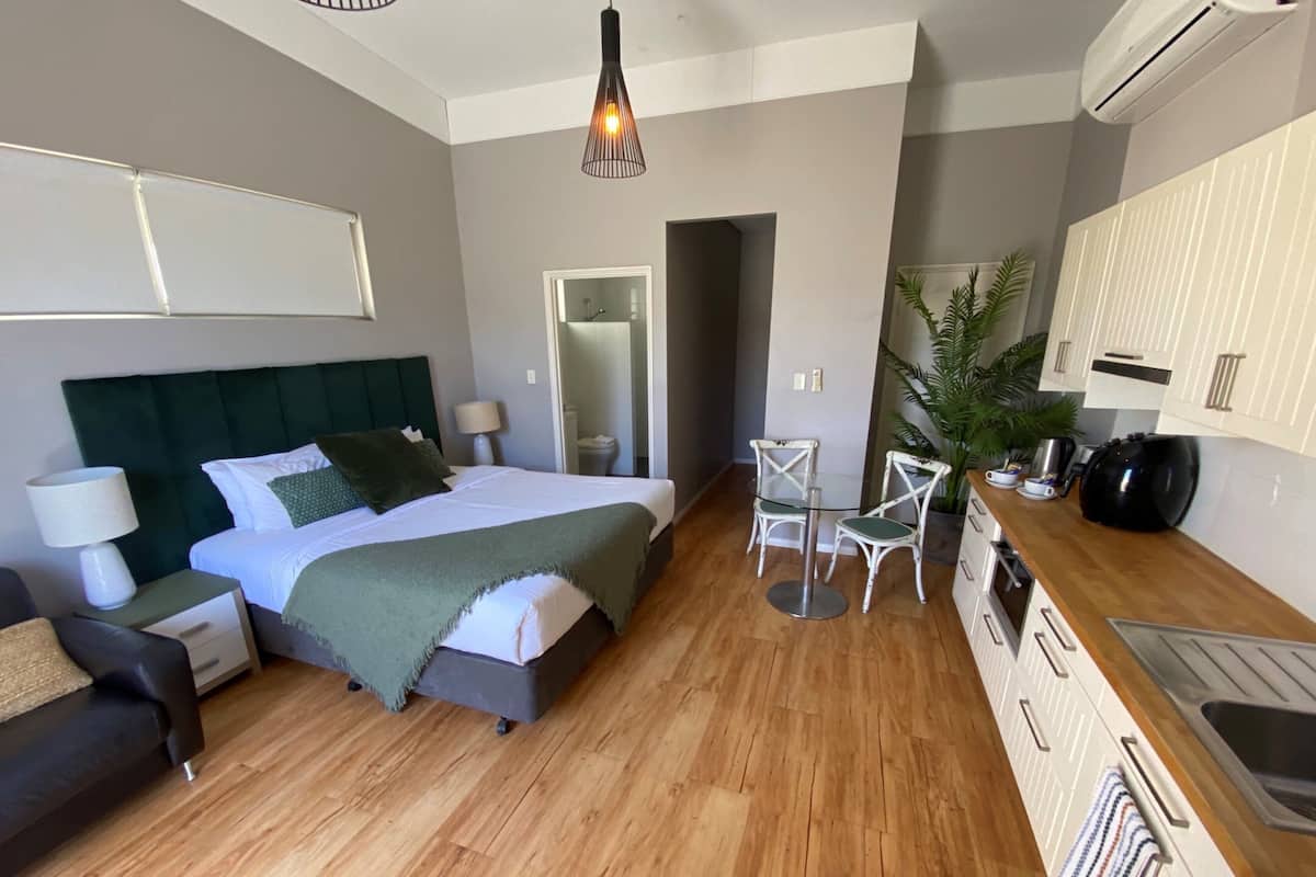Ein modernes Hotelzimmer mit Bett, Nachttisch, Lampe und einer kleinen Sitzecke mit Stühlen.