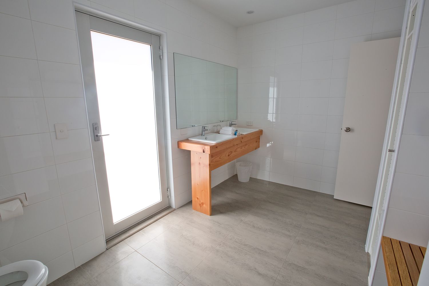A modern bathroom with a wooden vanity, white tiles, and a large mirror.