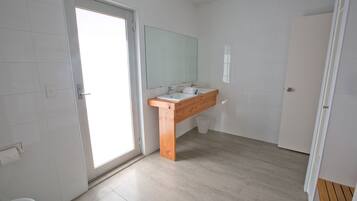 A modern bathroom with a wooden vanity, white tiles, and a large mirror.
