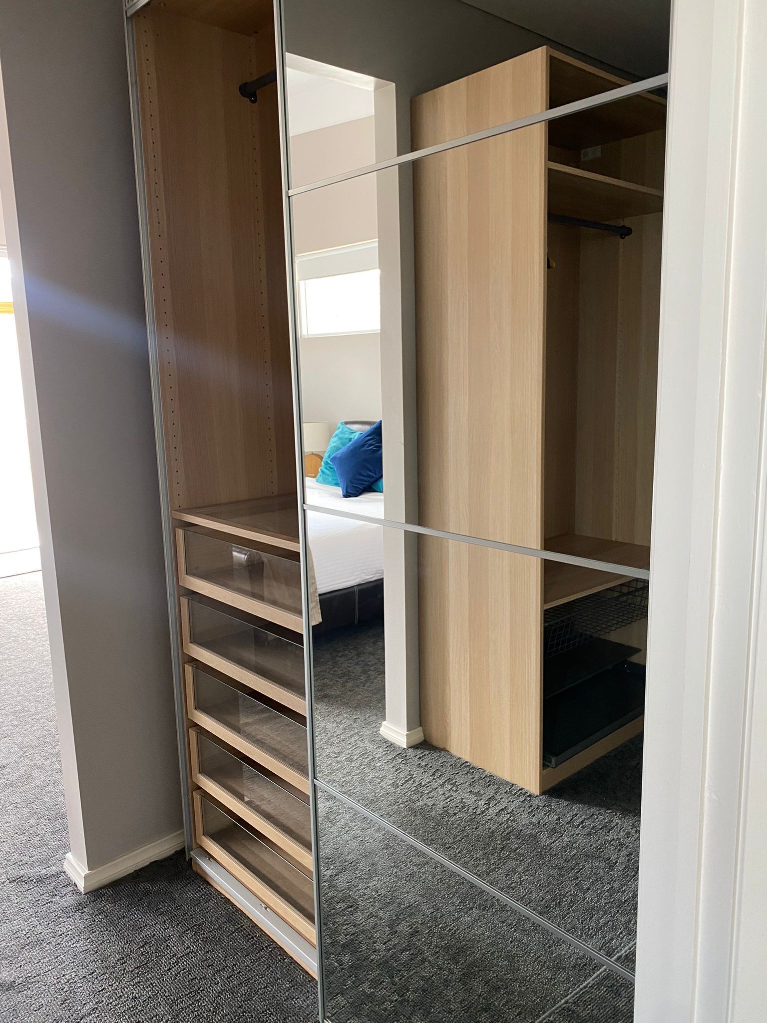 Ein begehbarer Kleiderschrank mit offenen Regalen, ein Bett mit blauen Kissen und ein grauer Teppichboden.