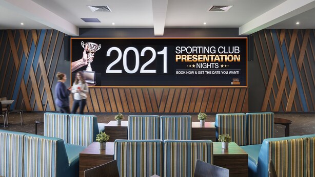 A modern lounge area with striped seating and a large presentation screen advertising a 2021 sporting club event.