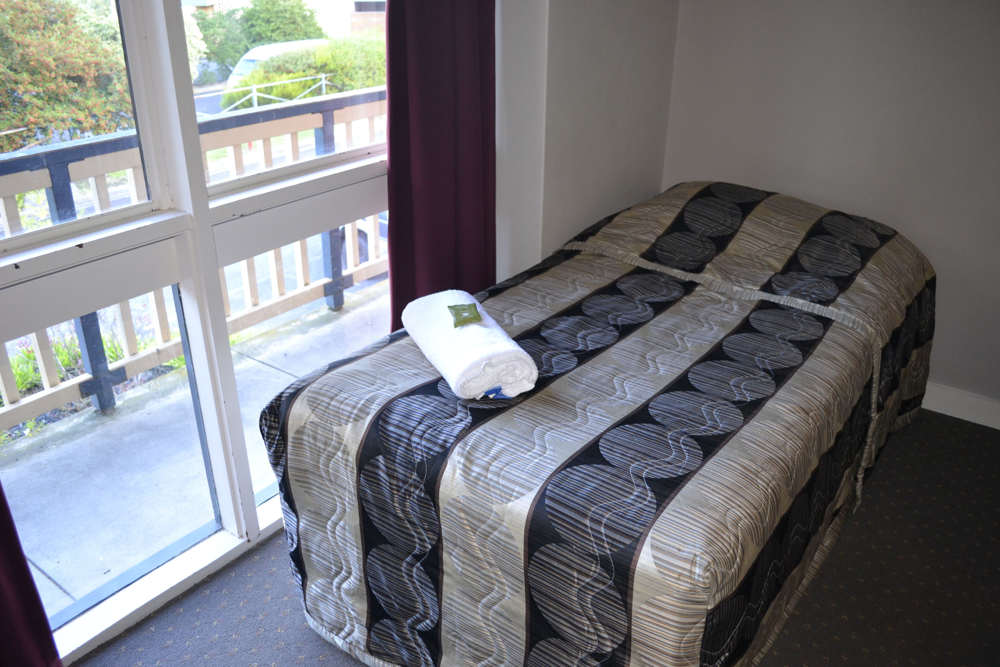 A bed with a patterned bedspread and a rolled-up towel on it.