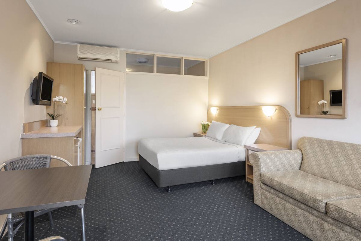 Een hotelkamer met een bed, een bank, een bureau, een televisie en een spiegel.