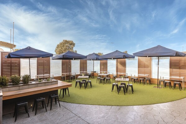 An outdoor patio with tables and chairs, umbrellas, and a green turf area. - Dorset Gardens Hotel (Croydon)
