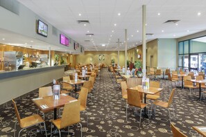 A spacious hotel dining area with multiple tables and chairs, a bar counter, and a large window providing natural light. - Dorset Gardens Hotel (Croydon)