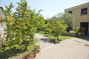 A courtyard with a paved walkway, potted plants, and a building with a stone facade. - Hotel Cala Mirto (Budoni)