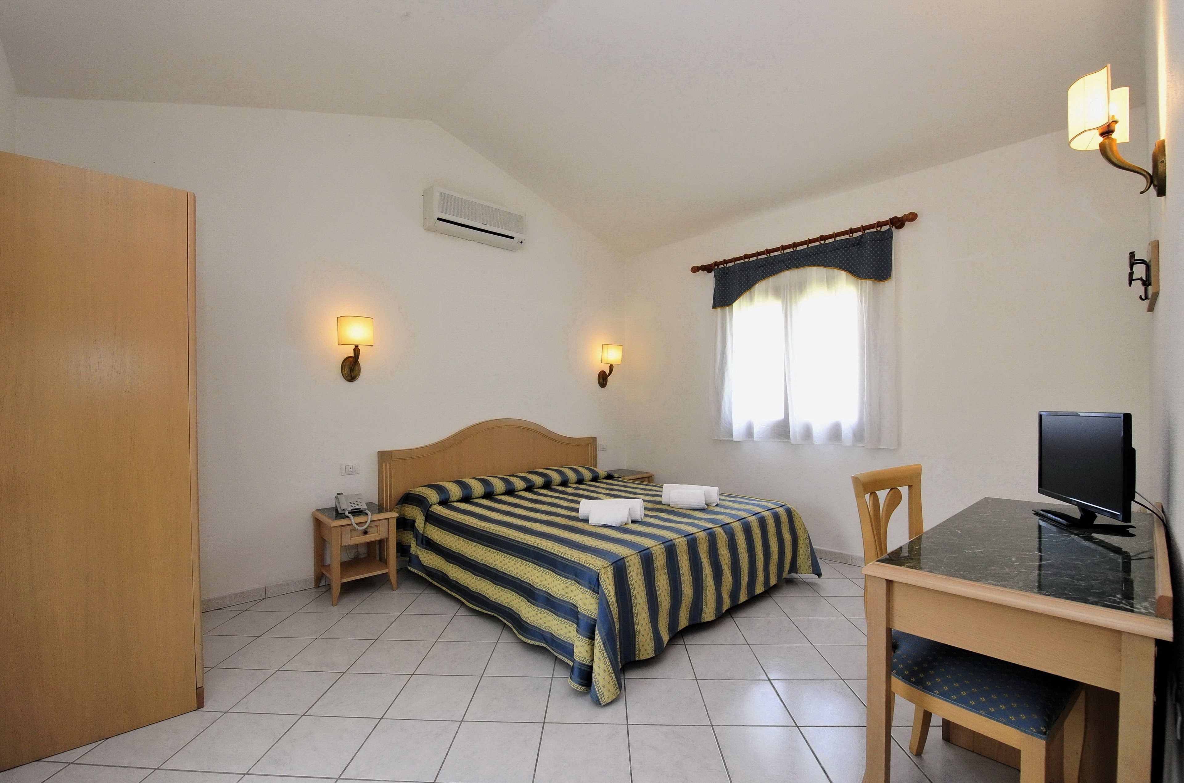 Habitación de hotel con cama, mesita de noche, lámpara, televisor y escritorio con silla.