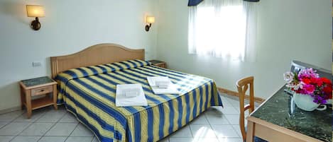 A hotel room with a bed, bedside tables, a desk with a chair, and a window with curtains.