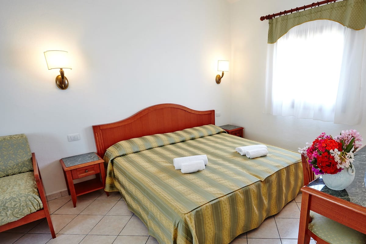 A neatly arranged hotel room with a bed, two bedside tables, a chair, a desk, and a window with curtains.