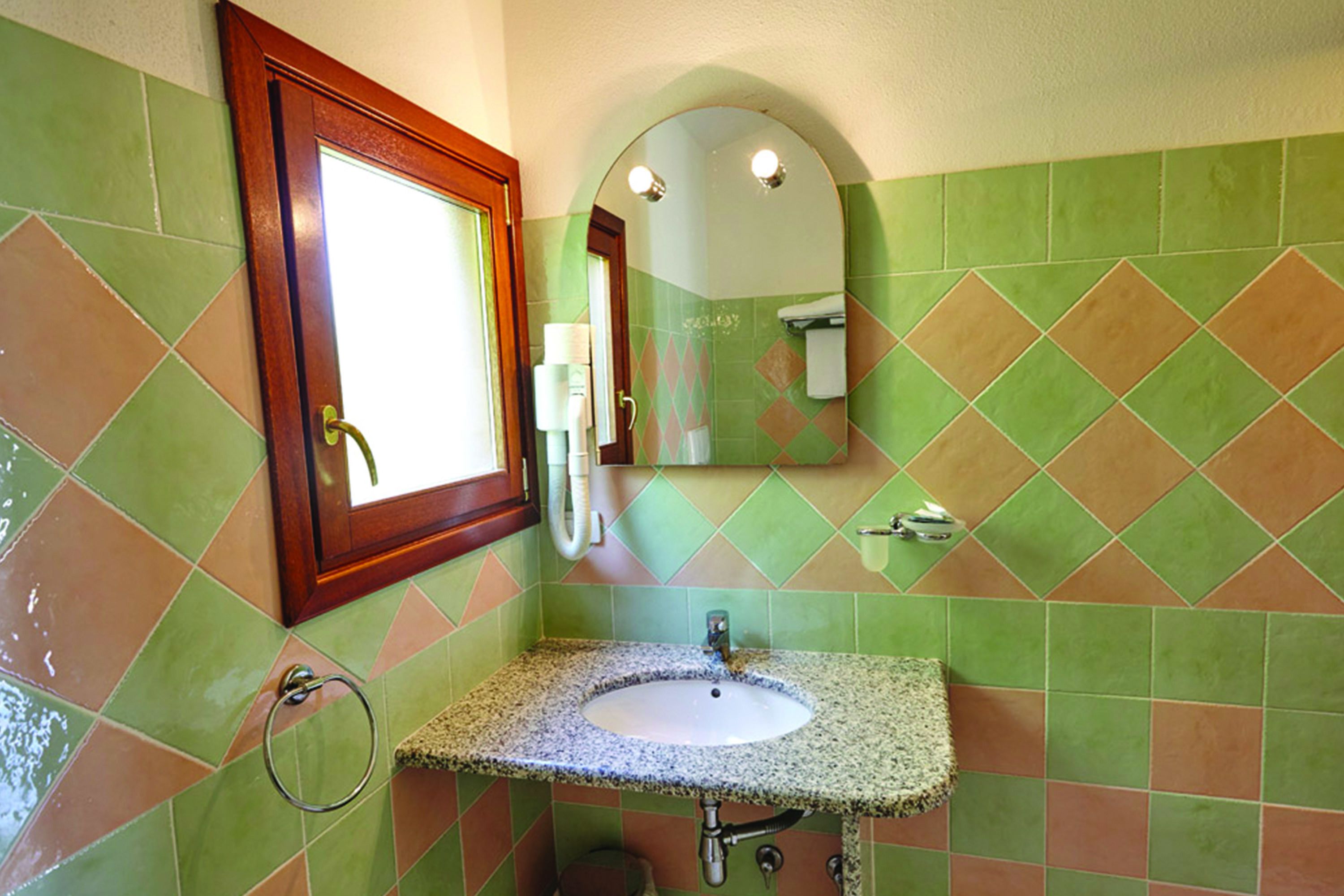 A bathroom with green and brown tiles, a sink with a granite countertop, a wooden-framed mirror, and a towel rack.