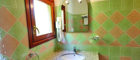 A bathroom with green and brown tiles, a sink with a granite countertop, a wooden-framed mirror, and a towel rack.