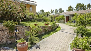 Un chemin pavé mène à un bâtiment dot é d’un toit en tuiles, entouré de verdure et de murs en pierre.