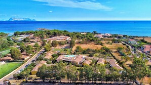 Vue aérienne d’un quartier résidentiel situé sur la côte, avec des maisons, une piscine et une vue dégagée sur la mer.