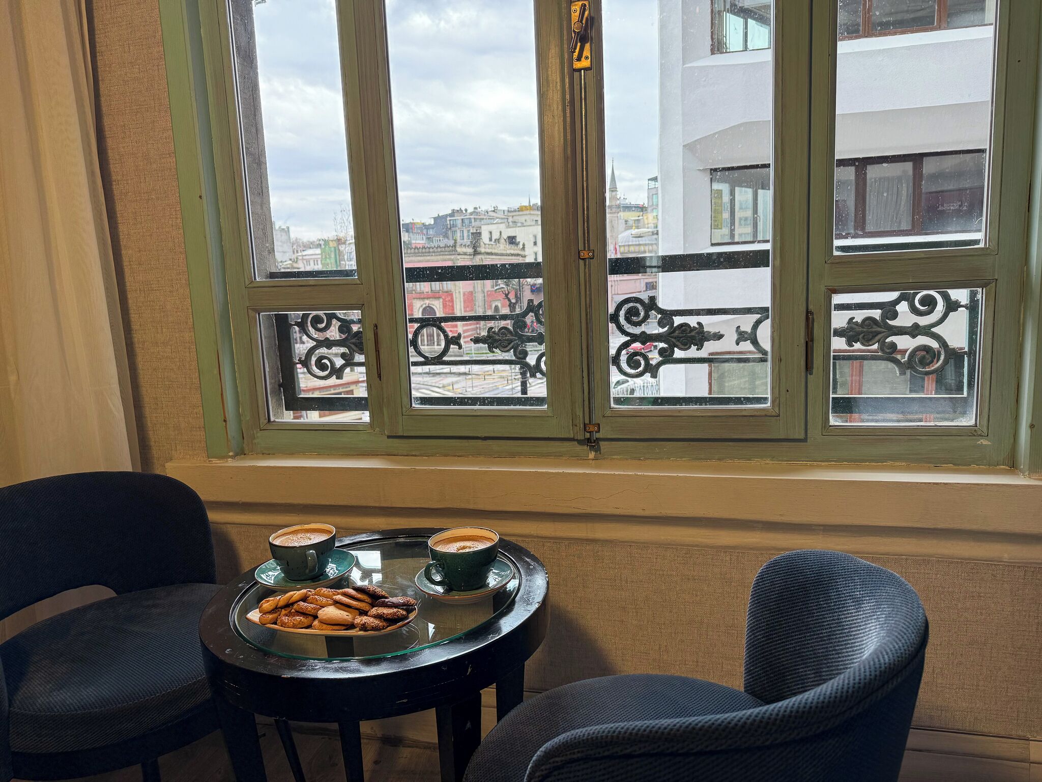Una habitación con una mesa dispuesta para dos personas, una ventana con rejas de hierro decorativas y vistas a edificios.