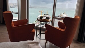 A room with two orange armchairs facing a large window overlooking a harbor with boats and a bridge. - Manesol Old City Bosphorus (Istanbul)