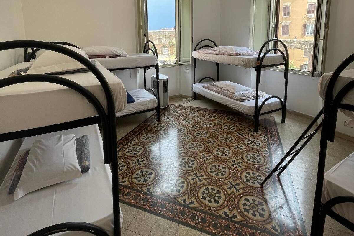A dormitory room with bunk beds, a patterned floor, and a view of buildings through open windows.