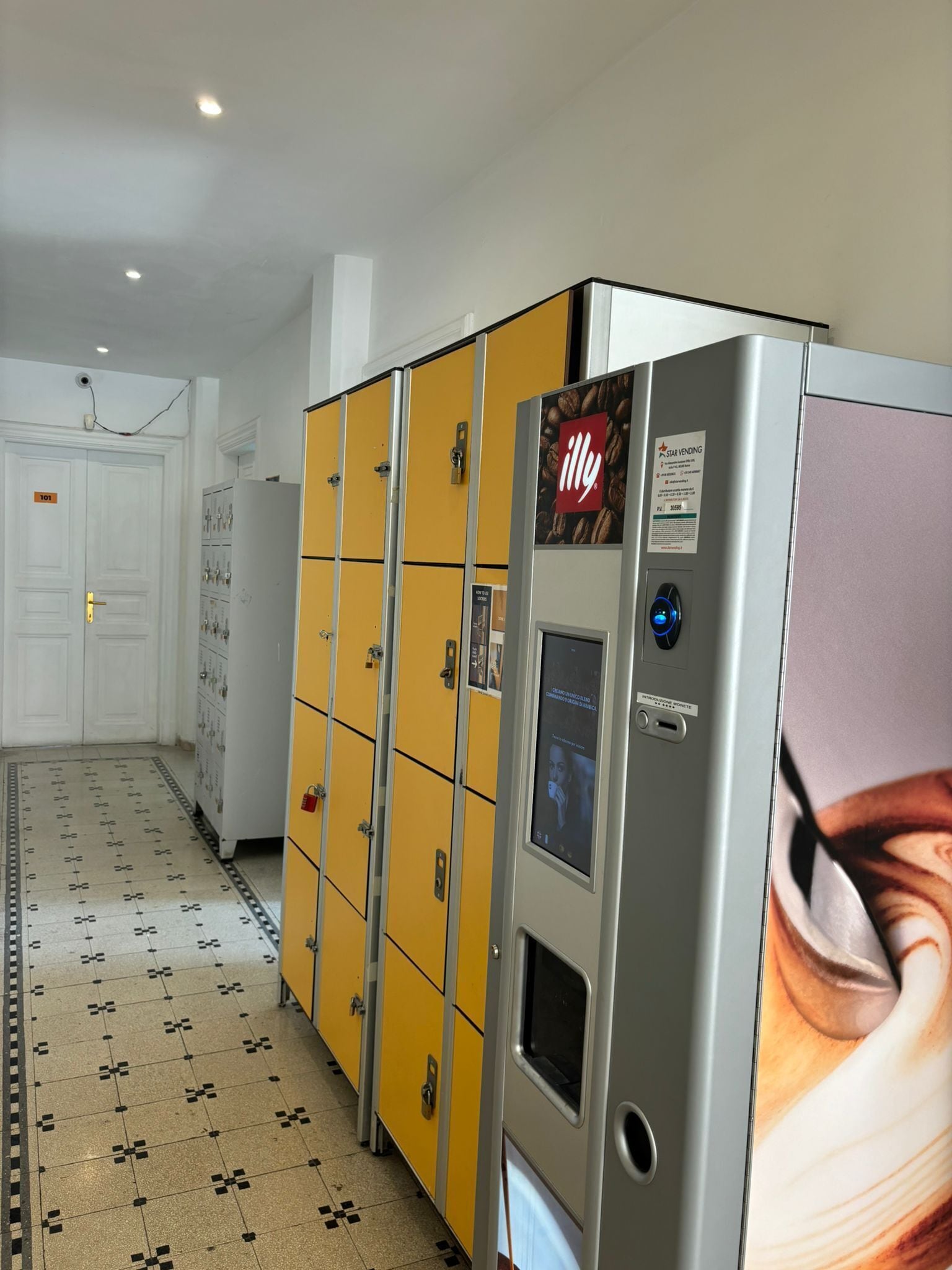 Un couloir d’hôtel avec des casiers, un distributeur automatique de la marque Star, et une porte portant le numéro 101.