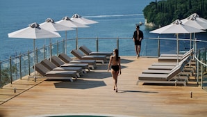 Une terrasse en bois avec des chaises longues et des parasols, donnant sur une étendue d’eau.