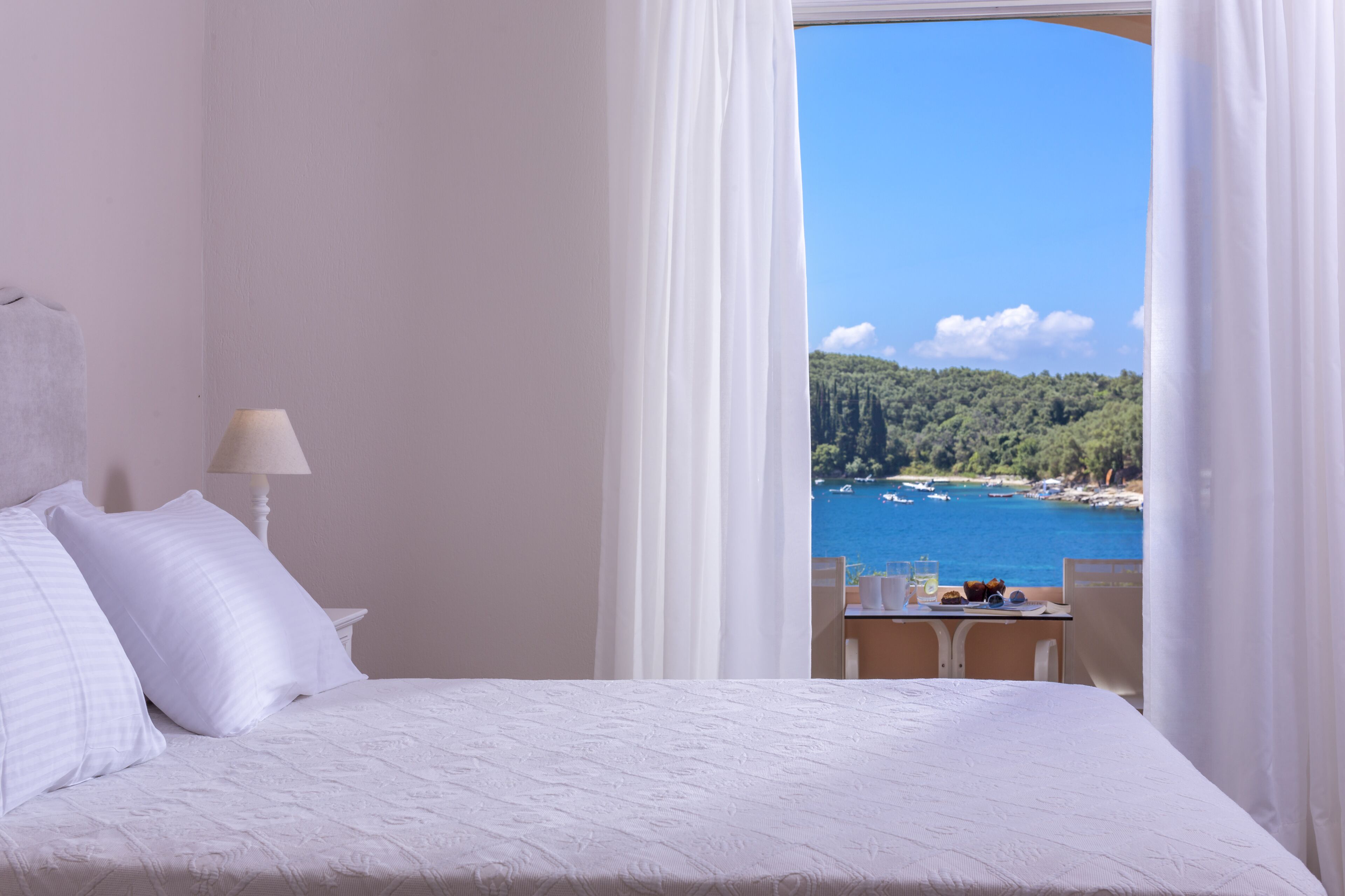 Ein Hotelzimmer mit Bett, Tisch mit einem Getränk und Blick auf das Meer.
