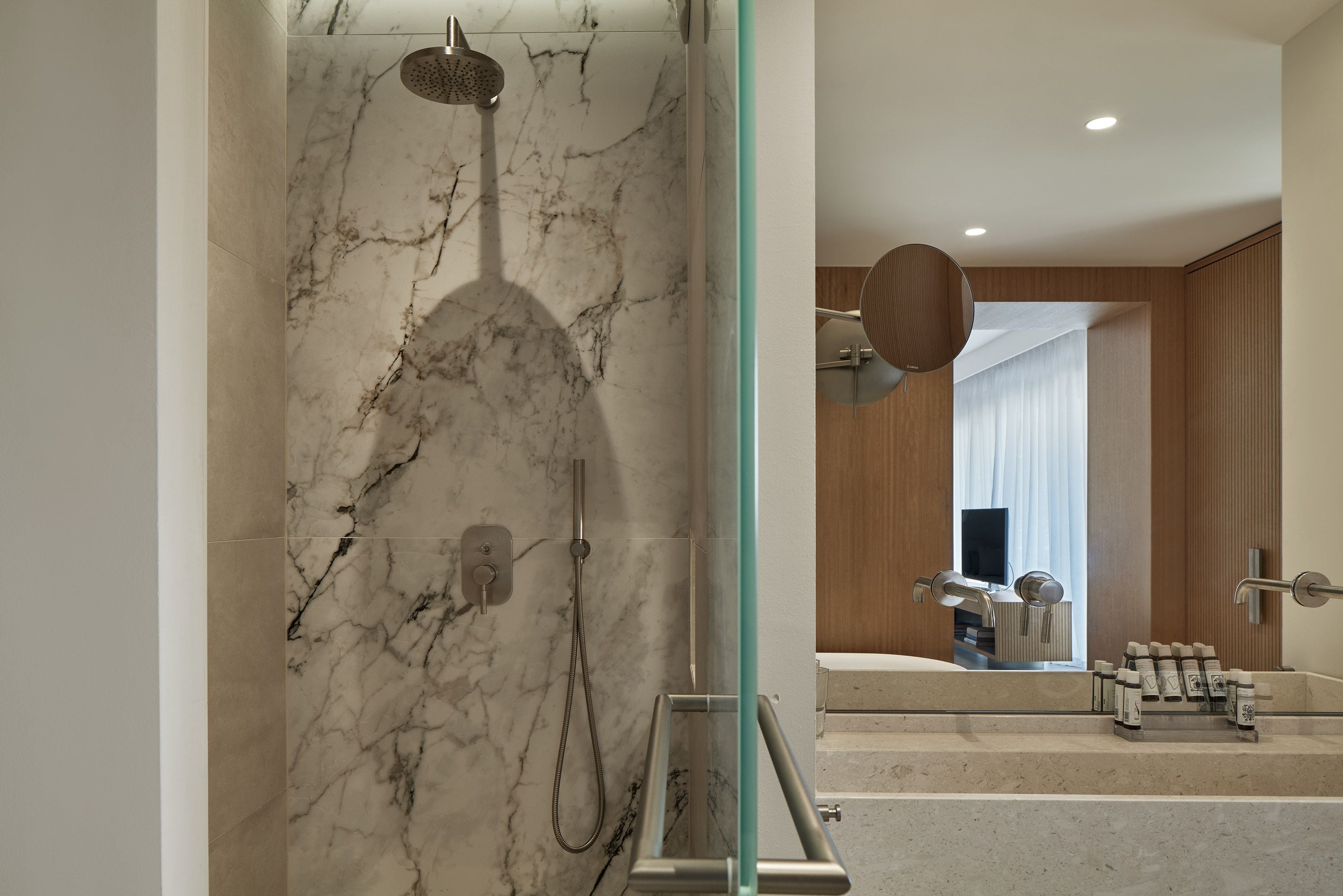A modern bathroom with a marble shower, a glass-enclosed shower area, a wooden vanity, and a large mirror.