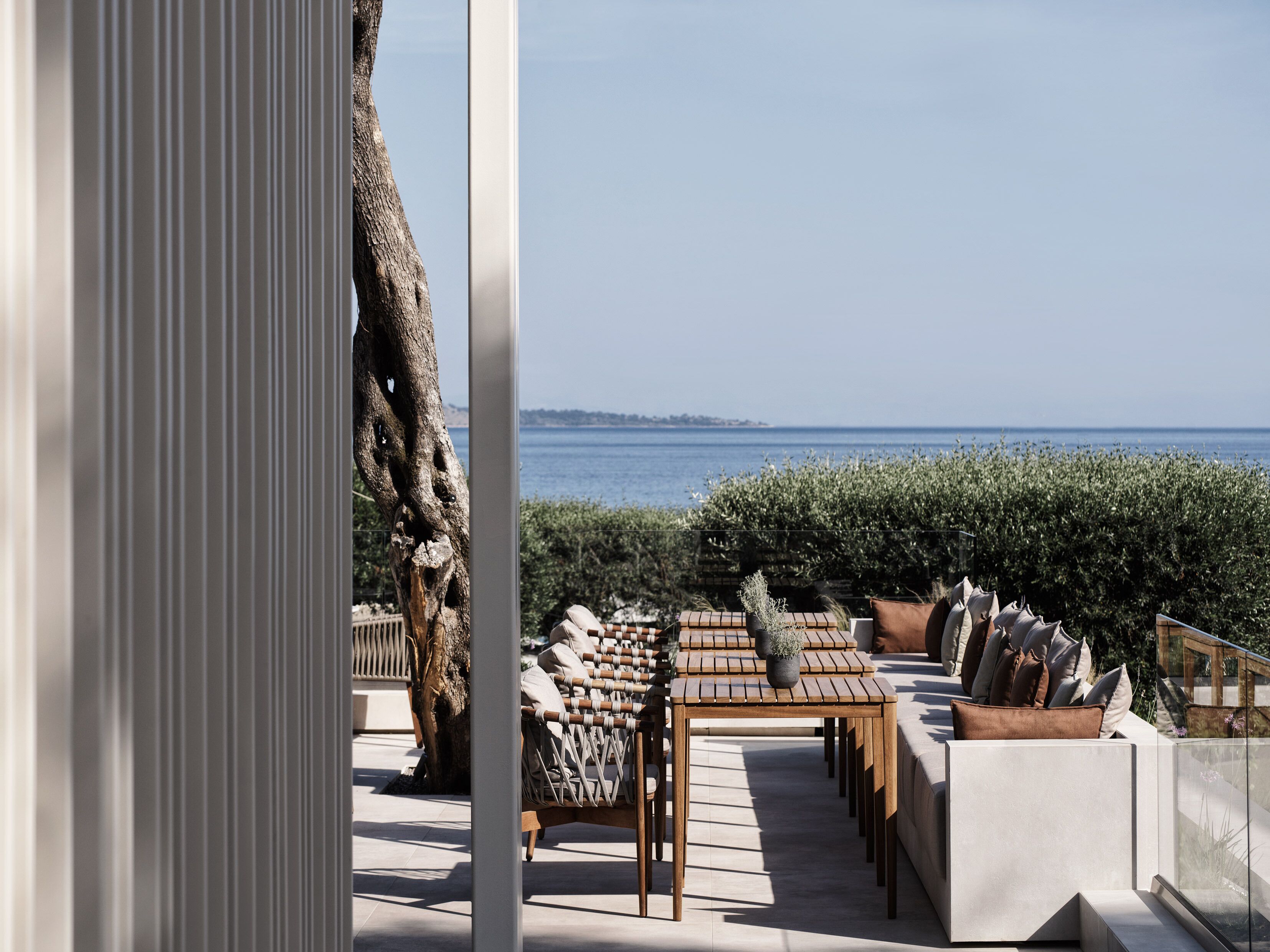 Ein Sitzbereich im Freien mit Blick aufs Meer, einem Holztisch und gepolsterten Sitzgelegenheiten.