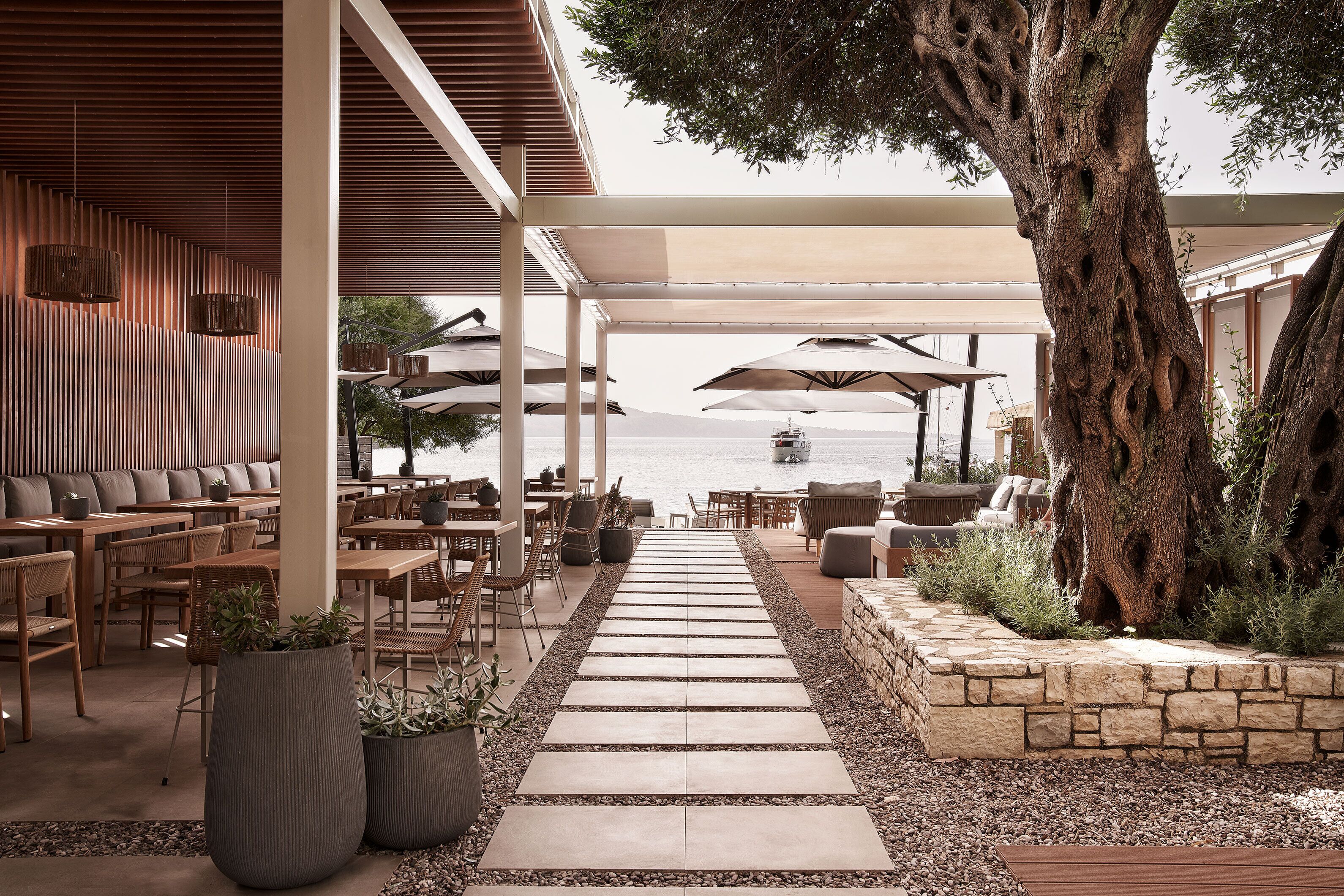 An outdoor seating area with tables and chairs, a stone pathway, and a large tree.