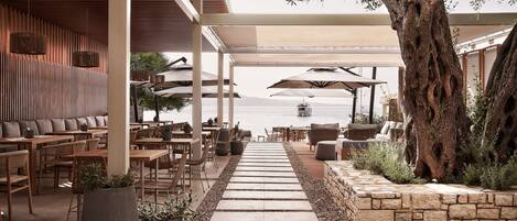 An outdoor seating area with tables and chairs, a stone pathway, and a large tree.