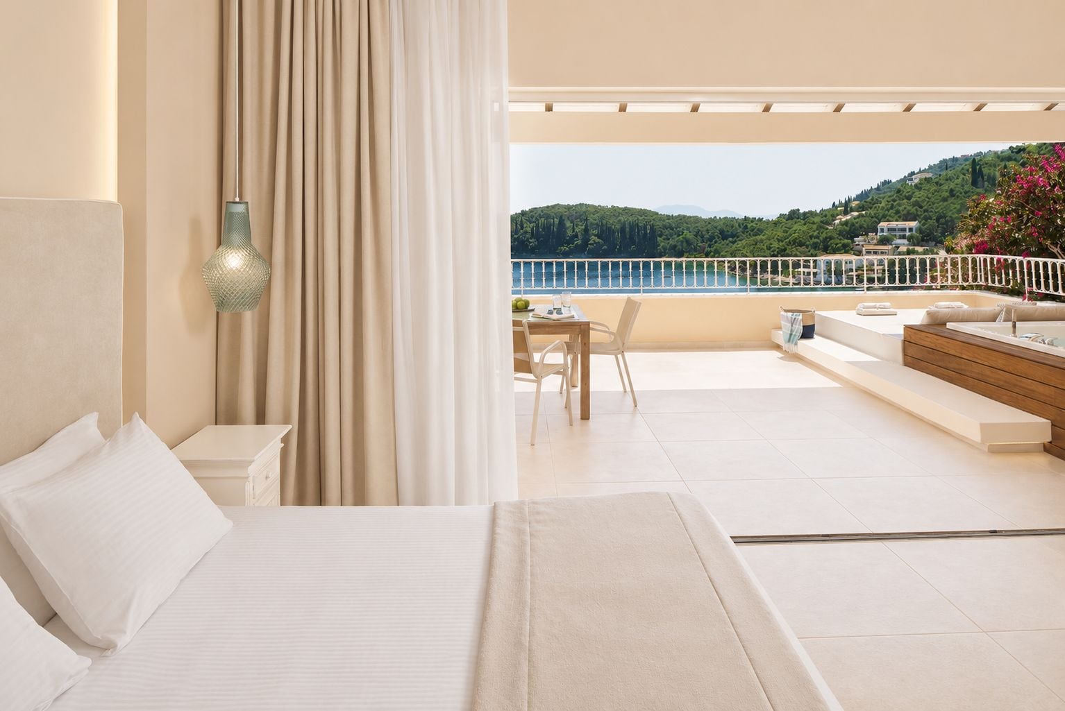 Habitación de hotel con cama, escritorio y balcón con vista a una colina y un cuerpo de agua.