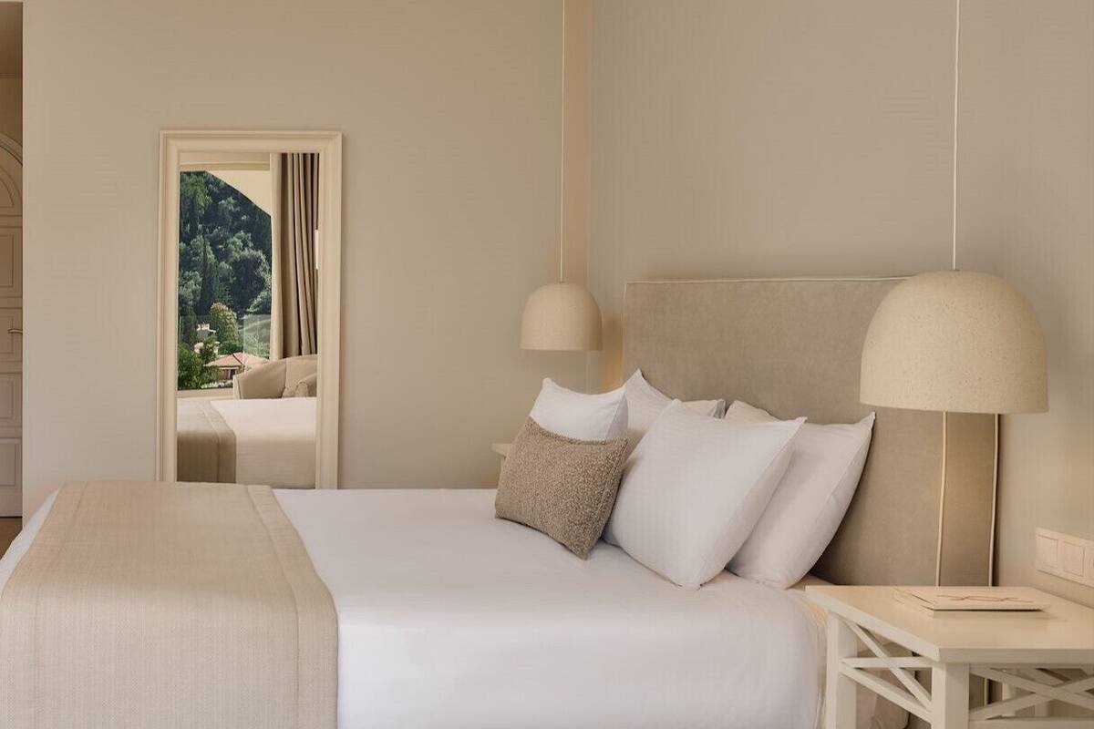 Hotelkamer met een groot bed, twee bedlampjes, een nachtkastje en uitzicht op een bergachtig landschap door een deuropening.