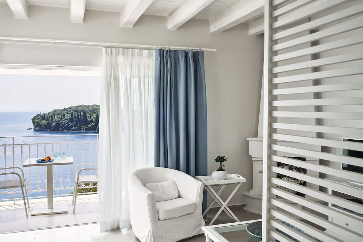 Een balkon met een witte stoel, een klein tafeltje met een blauw bord en een bloempot.
