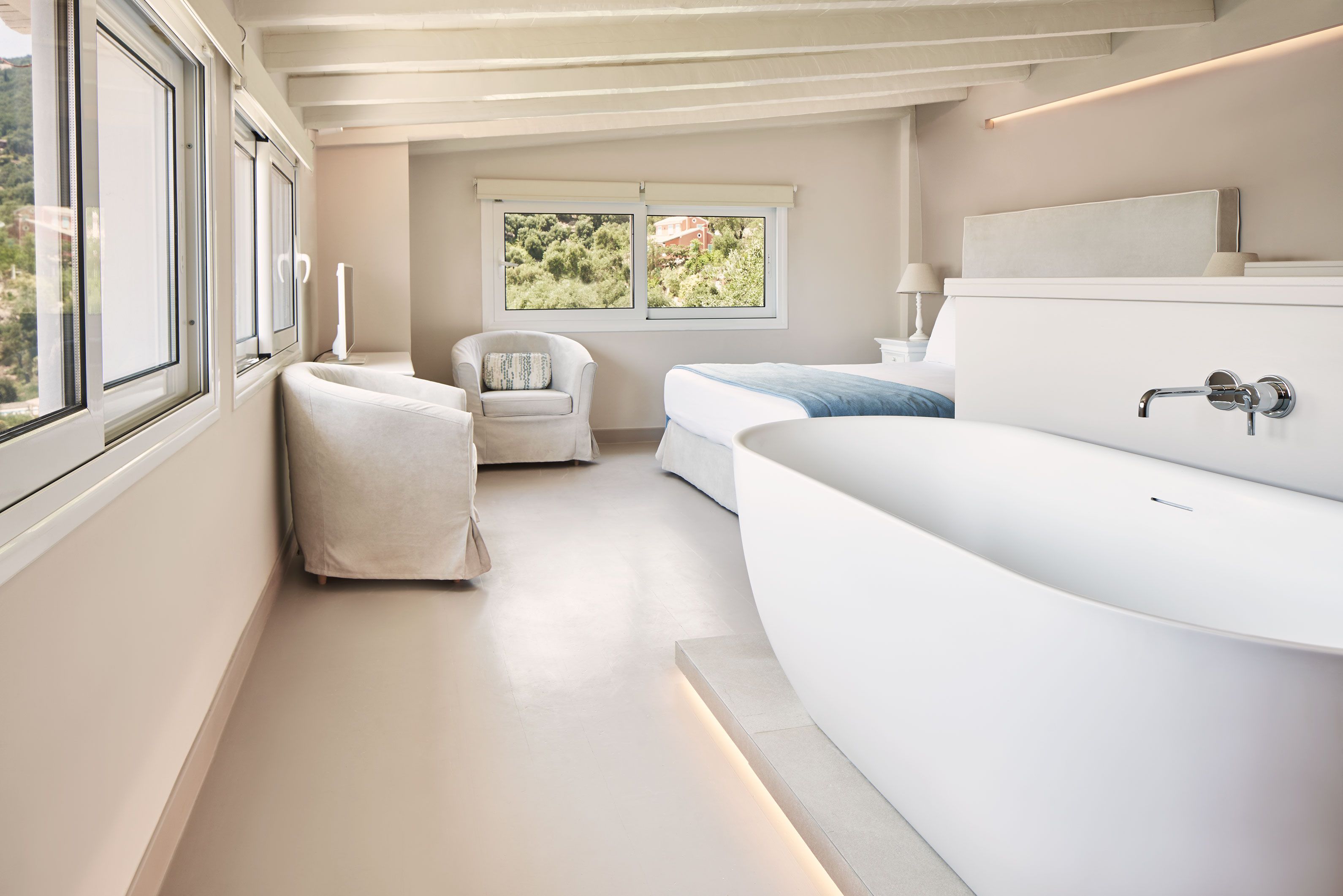 Un bagno moderno con una vasca da bagno ampia, una sedia e una finestra vista verde.
