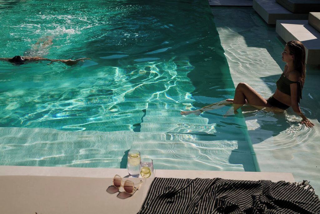 Una piscina con agua cristalina, una persona nadando y otra sentada en el borde.