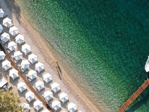 Vue aérienne d’une plage avec une eau cristalline, des parasols et une promenade en bois.
