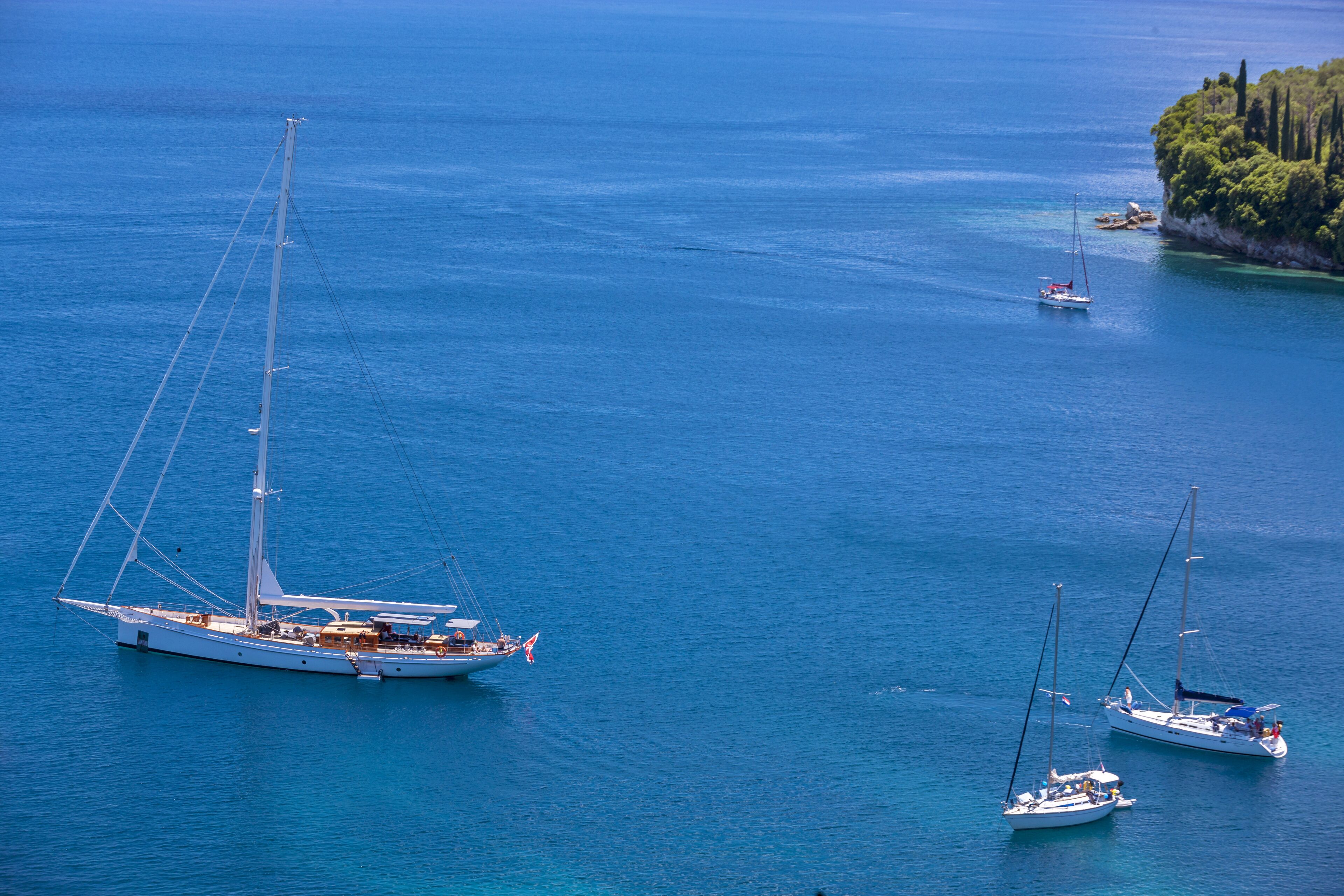 A large yacht anchored in calm waters with a small island in the background.