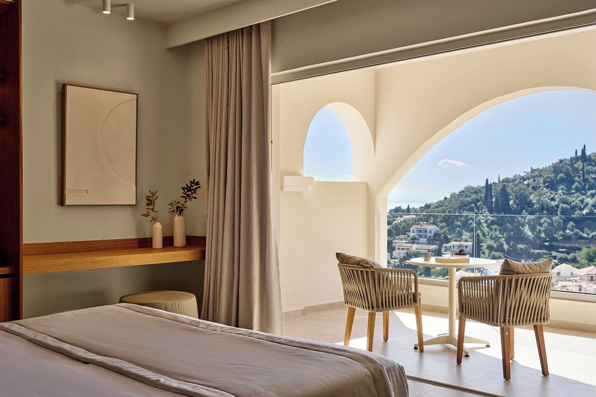 Une chambre à coucher comprenant un lit, une table de chevet, une fenêtre avec des rideaux, un balcon avec des chaises et une vue sur une colline.