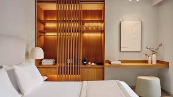 Een moderne hotelkamer met een net opgemaakt bed, een houten garderobe met ingebouwde verlichting, een nachtkastje met lamp en een klein zithoekje.