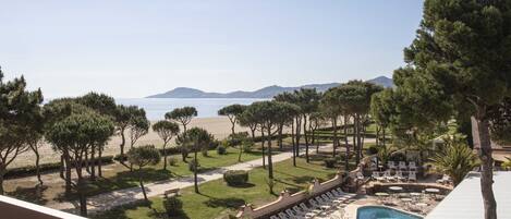 A pool area with lounge chairs and a view of the beach and mountains.